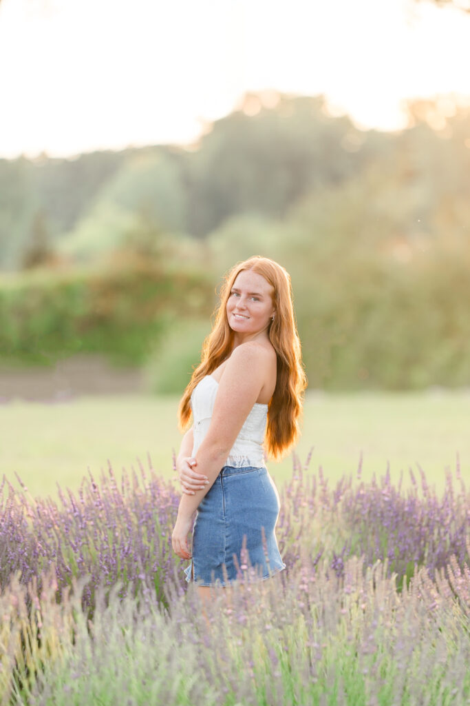 Senior girl in a white dress standing in a lavender field in Mid Michigan during golden hour.