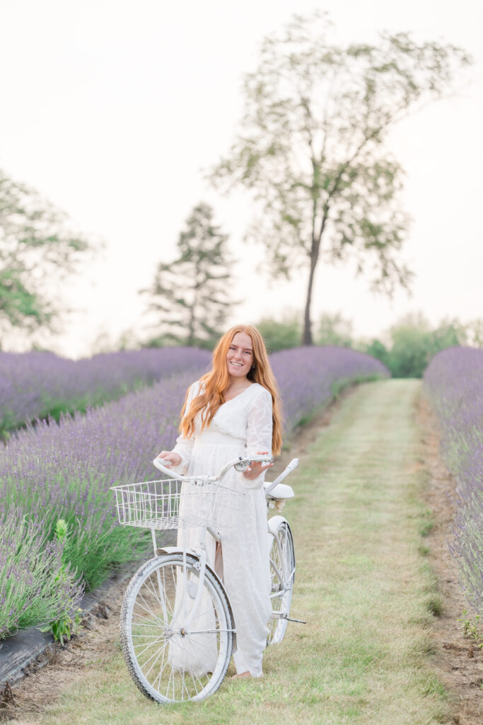 Senior girl in a white dress standing in a lavender field in Mid Michigan during golden hour.