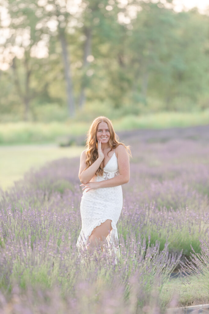 Senior girl in a white dress standing in a lavender field in Mid Michigan during golden hour.
