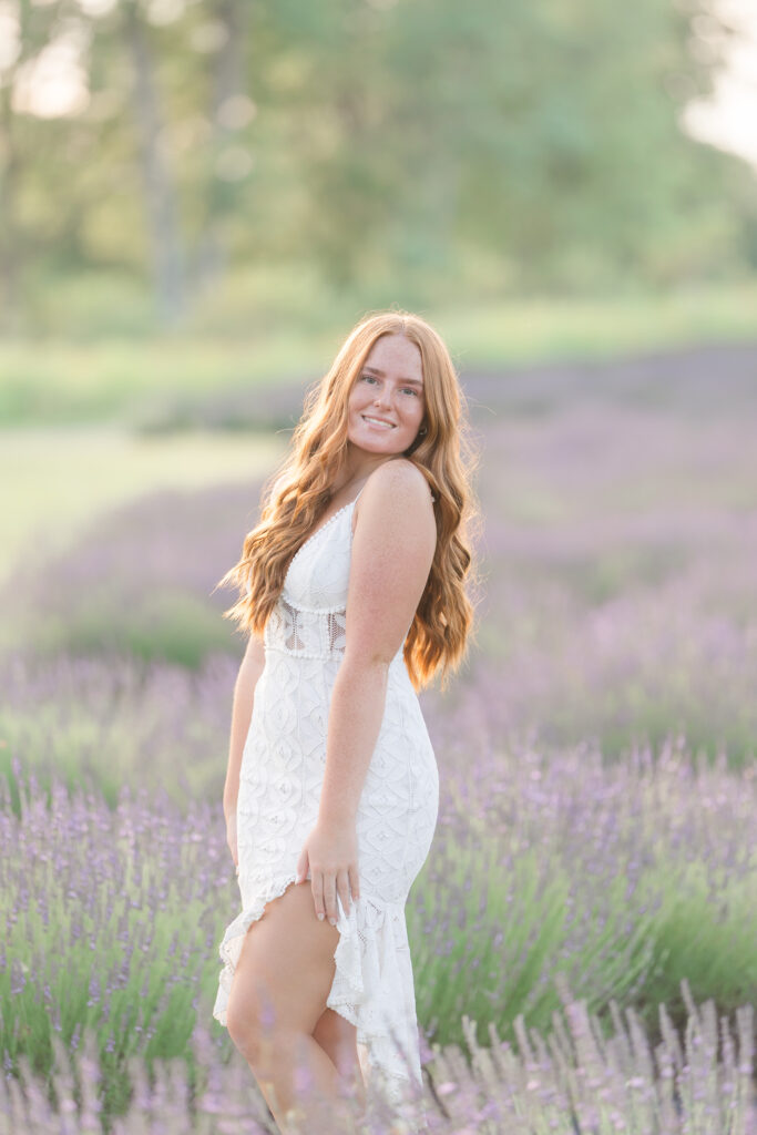 Senior girl in a white dress standing in a lavender field in Mid Michigan during golden hour.